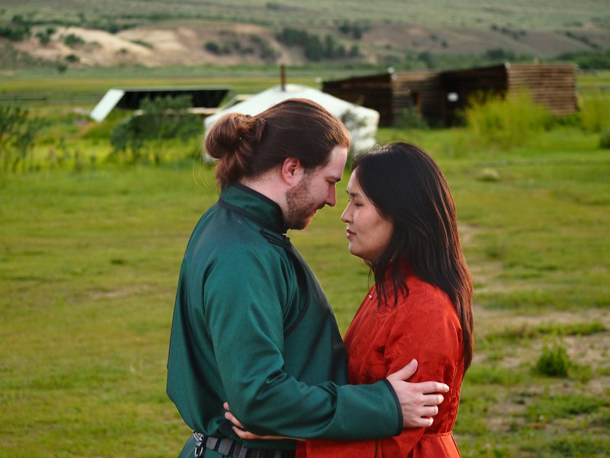 Couple embracing in a green field with distant structures.